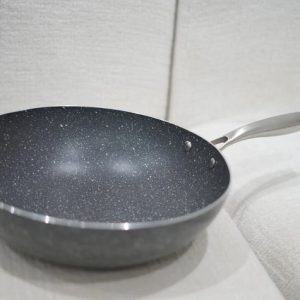Dark grey, speckled non-stick wok or deep frying pan with a long, polished stainless steel handle on a white textured surface.
